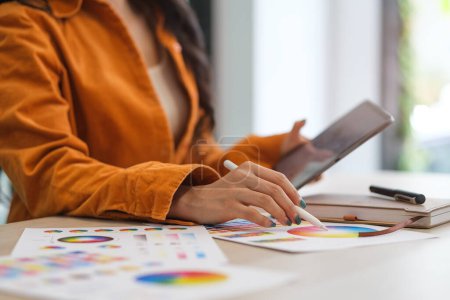 Foto de Imagen recortada del diseñador femenino sosteniendo la tableta digital, trabajando con muestras de color en el escritorio. - Imagen libre de derechos