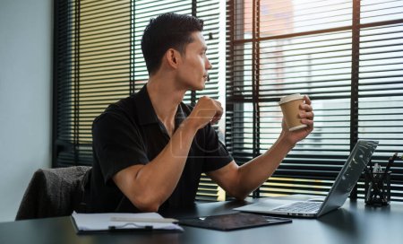 Téléchargez les photos : Relaxed asian man holding coffee and looking away while sitting in modern office. - en image libre de droit