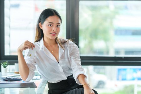Photo for Portrait of millennial businesswoman in white shirt sitting at desk and looking at camera. - Royalty Free Image