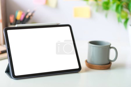 Téléchargez les photos : Tablette numérique avec écran vide sur tasse à café et bloc-notes sur bureau blanc. Copiez l'espace pour votre texte. - en image libre de droit