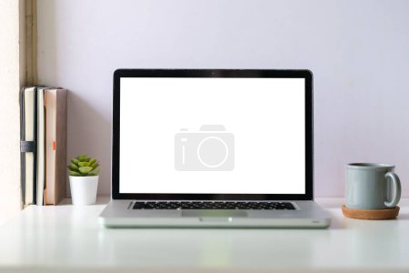 Foto de Escritorio blanco con portátil, taza de café y libros. Espacio de trabajo moderno, pantalla en blanco para su texto publicitario. - Imagen libre de derechos