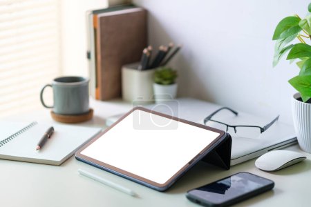 Photo for Modern workspace with a tablet computer, pot plant, notebook and coffee cup on white desk. Blank screen monitor for graphic display montage. - Royalty Free Image