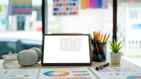 Téléchargez les photos : Tablette numérique avec écran blanc vide, casque, échantillons de couleur et papeterie sur l'espace de travail du graphiste. - en image libre de droit