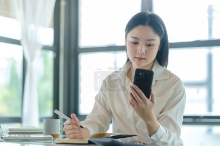 Foto de Empleadas asiáticas revisando redes sociales, leyendo noticias en línea en su teléfono inteligente. - Imagen libre de derechos