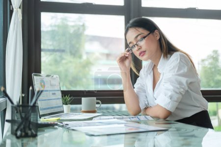 Téléchargez les photos : Femme d'affaires sérieuse assise devant un ordinateur portable sur son lieu de travail et lisant des rapports financiers. - en image libre de droit