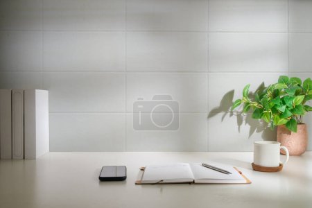 Foto de Espacio de trabajo mínimo con libro, taza de café y portalápices sobre mesa blanca. Copia espacio para tu texto publicitario. - Imagen libre de derechos