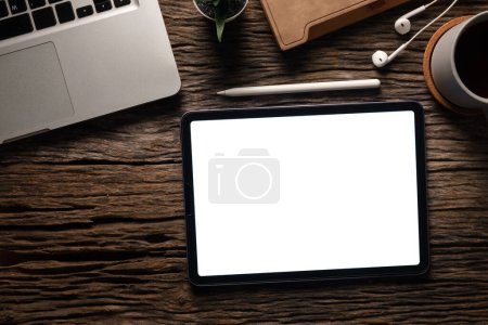 Foto de Tableta digital con pantalla blanca, portátil, taza de café, portátil y auriculares en mesa de madera. - Imagen libre de derechos