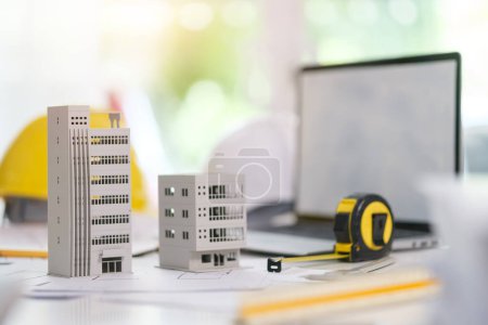 Photo for Architectural model of residential  on desk with laptop, drawing technical tools and blueprints. Real estate business, building and construction. - Royalty Free Image
