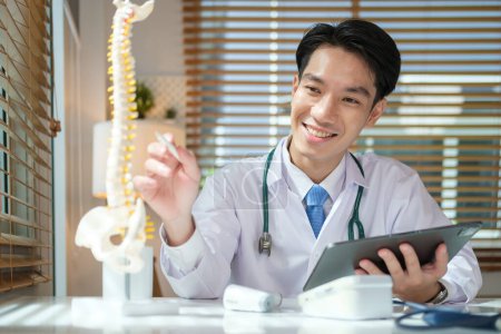 Téléchargez les photos : Orthopédiste masculin tenant tablette numérique et pointant vers le modèle de la colonne vertébrale humaine. Concept médical, orthopédique et de santé. - en image libre de droit