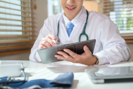 Foto de Médico con bata blanca y estetoscopio usando tableta digital en la clínica. Concepto médico y sanitario. - Imagen libre de derechos