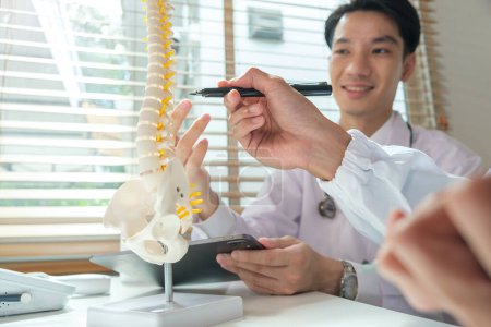 Foto de Ortopedistas apuntando al modelo de columna vertebral hablando del diagnóstico de los pacientes en el consultorio médico. - Imagen libre de derechos