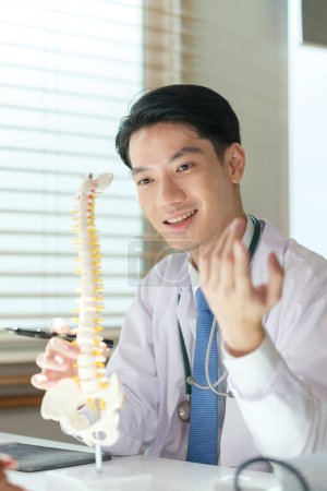 Foto de Cirujano ortopédico masculino mostrando columna artificial, explicando el curso del tratamiento, dando consejos de recuperación al paciente. Concepto médico, ortopédico y sanitario. - Imagen libre de derechos