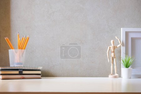 Photo for Creative workspace with blank poster frame, coffee cup, books and flower pot on white table. - Royalty Free Image
