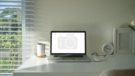 Photo for Laptop computer with blank display, potted plant, picture frame and stationery on white table. - Royalty Free Image