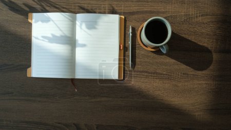 Foto de Cuaderno plano, taza de café y planta en maceta en escritorio de oficina de madera. - Imagen libre de derechos