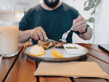 Téléchargez les photos : A man is eating chicken grilled served on the plate at a cafe. - en image libre de droit