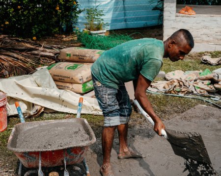Téléchargez les photos : Selangor, Malaisie - 21 octobre 2023Un homme mélange du béton avec une pelle sur le sol à la main dans une construction de rénovation de maison. - en image libre de droit