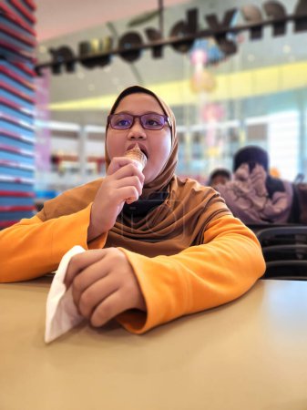 Téléchargez les photos : Le jeune enfant portant du hijab mange de la glace au centre commercial. - en image libre de droit