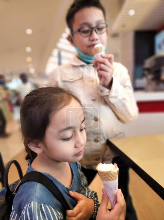 Téléchargez les photos : Les enfants mangent de la glace au centre commercial. Petite fille et grand frère dégustant des desserts. - en image libre de droit