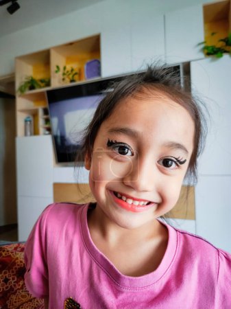 Portrait of a cute Asian little girl with funny eyeliner make up on her face smiling.