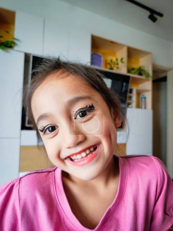 Téléchargez les photos : Portrait d'une mignonne petite fille asiatique avec eye-liner drôle maquillage sur son visage souriant. - en image libre de droit