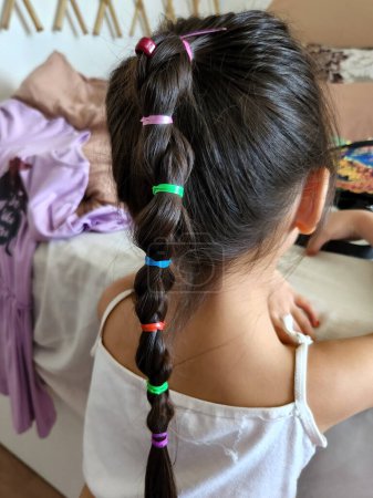 Young girl with colourful braided hair from behind.