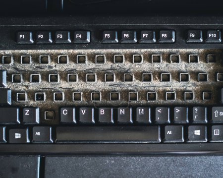 Schmutzige Qwerty-Tastatur voller Staub und Unrat auf dem Tisch. Reinigung des Computers.