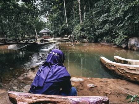 Téléchargez les photos : Femme hijab regardant le ruisseau près de la jungle de la forêt tropicale. - en image libre de droit