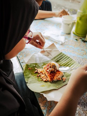 Téléchargez les photos : Manger de la nourriture asiatique nasi lemak sur feuille de banane comme petit déjeuner, vue arrière. - en image libre de droit