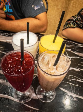 Téléchargez les photos : Diverses boissons glacées servies dans un grand verre avec des pailles en plastique sur une table en marbre. - en image libre de droit