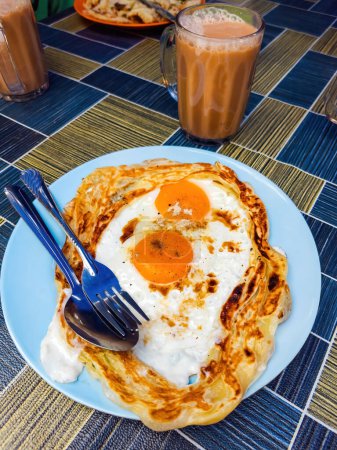 Roti sarang burung, eine Pratha sieht aus wie ein Vogelnest mit halb gekochten Eiern in der Mitte, serviert mit Tarik als Hauptfrühstück in Malaysia.