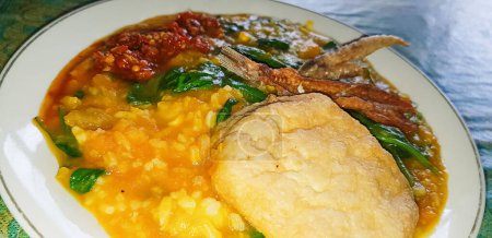 Foto de Tinutuan, bubur manado, plato tradicional indonesio de gachas mezclado de arroz, calabaza y verdura kangkung servido con pescado salado y sambal - Imagen libre de derechos