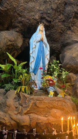 Foto de Estatua de la Santísima Virgen María en la Iglesia Católica Romana, en la cueva de la Virgen María, en una capilla cueva de roca Iglesia Católica con flores tropicales alrededor en el asiático - Imagen libre de derechos