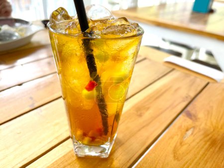 frisch gemixter Fruchtcocktail-Alkohol-Drink mit Rum und Whiskey in einem klaren Glas und Eisbrocken auf einem hölzernen Tischhintergrund