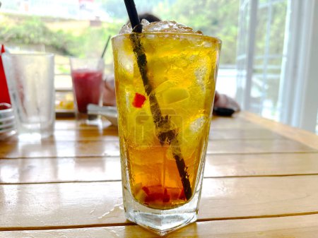 mezcla fresca bebida alcohólica cóctel de frutas con ron y whisky en un vaso transparente y trozo de hielo sobre un fondo de mesa de madera