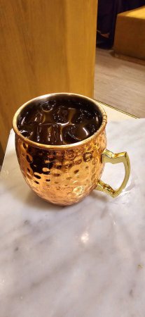 Traditional iced tea served in a unique and artistic brass cup , ice tea garnished with rosemary twigs in a restaurant