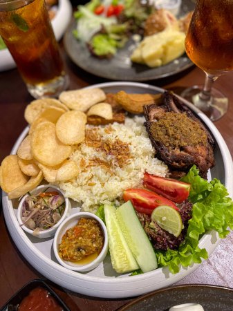 Nasi uduk ayam bakar, or coconut milk flavor rice served with grilled chicken, fresh salad, and chili paste traditional Indonesian food, indonesian street food, homemade food