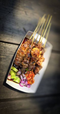 Photo for Lamb grilled satay served with barbecue savory sauce and pickled onion, chili and cucumber, selective focus photo on top of wooden table - Royalty Free Image