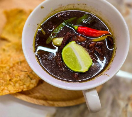Rawon or Indonesian black beef soup, black color are from indonesian nut called kluwek. Served with lime, chili paste, salted egg, and tempe cracker. Perfect for recipe, article, or any cooking contents or blog