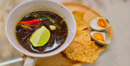 Soupe de b?uf noir rawon ou indonésien, de couleur noire sont de noix indonésienne appelée kluwek. Servi avec du citron vert, de la pâte de chili, des ?ufs salés et du biscuit tempéré. Parfait pour la recette, l'article, ou tout contenu de cuisine ou blog
