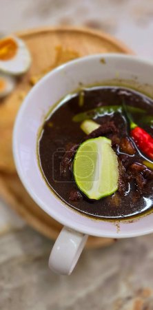 Soupe de b?uf noir rawon ou indonésien, de couleur noire sont de noix indonésienne appelée kluwek. Servi avec du citron vert, de la pâte de chili, des ?ufs salés et du biscuit tempéré. Parfait pour la recette, l'article, ou tout contenu de cuisine ou blog