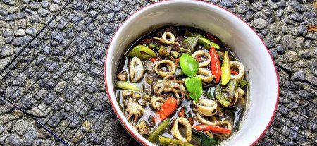 Indonesian home cooking menu, sauteed squid with black ink sauce with spicy seasoning called Tumis Cumi Hitam, including chili, ginger, and lime leaf served in a bowl