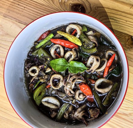 Indonesian home cooking menu, sauteed squid with black ink sauce with spicy seasoning called Tumis Cumi Hitam, including chili, ginger, and lime leaf served in a bowl