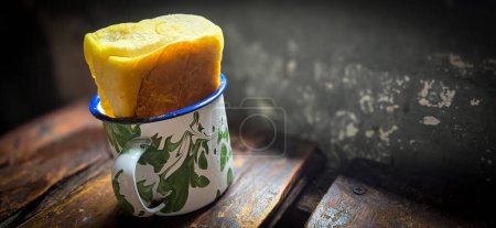 Ice chocolate drink on a vintage Indonesian iron mug with random green pattern called Blirik cup or cangkir Blirik on bokeh background along with chocolate filling bread on a cafe in Bogor