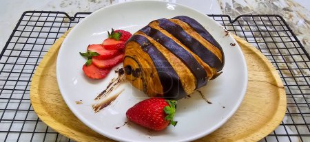 Photo for Fresh homemade striped chocolate croissant with chocolate filling on a round white plate, served with fresh strawberry, good cooking ideas - Royalty Free Image