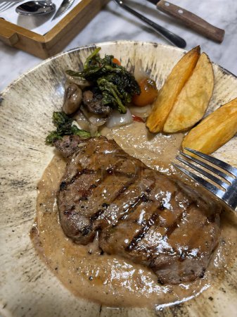 Steak de surlonge grillé moyen rare servi avec pommes de terre et salade avec sauce au poivre noir aux champignons dans un restaurant