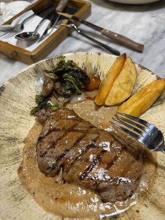 Steak de surlonge grillé moyen rare servi avec pommes de terre et salade avec sauce au poivre noir aux champignons dans un restaurant
