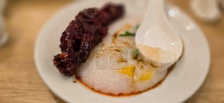 Reisbrei mit geschreddertem Huhn Bubur Ayam genannt, serviert mit Crackern und in Scheiben geschnittenen Frühlingszwiebeln und anderen Gewürzen im Restaurant