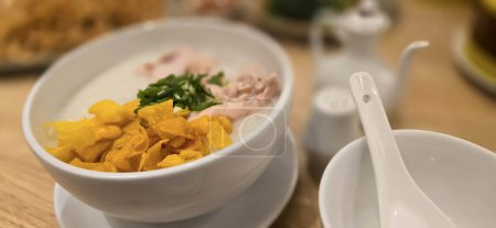 avena de arroz con pollo rallado llamado bububur ayam servido con galletas saladas y cebolla en rodajas de primavera y otros condimentos en el restaurante