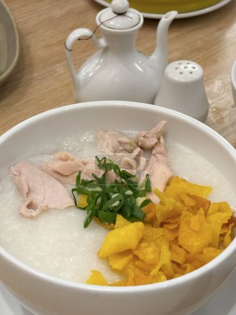 bouillie de riz avec poulet râpé appelé bubur ayam servi avec des craquelins et des tranches d'oignon de printemps et d'autres condiments dans le restaurant
